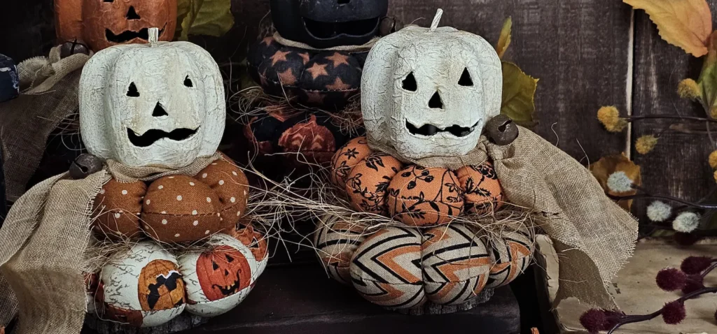 Primitive Jack‑O‑Lantern stack with Antique White head on Halloween fabric cushions and real wood slice base