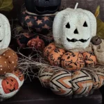 Primitive Jack‑O‑Lantern stack with Antique White head on Halloween fabric cushions and real wood slice base
