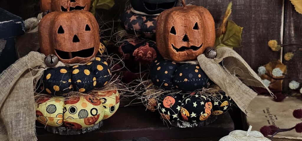 Primitive Jack‑O‑Lantern stack with Autumn Orange head on fabric cushions and real wood slice base.