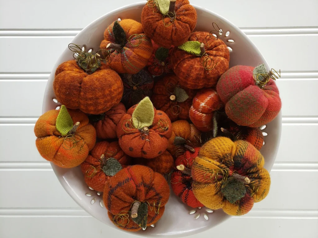 Close‑up of a bowl filled with mini flannel woolies pumpkins showing stitched details, wool leaves, and rustic fall colors