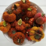 Close‑up of a bowl filled with mini flannel woolies pumpkins showing stitched details, wool leaves, and rustic fall colors