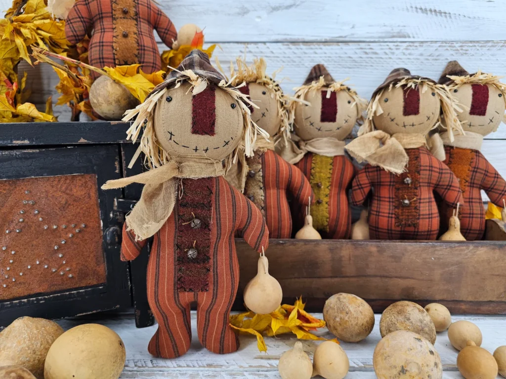 Group of primitive folk art scarecrow dolls with stitched faces, wool noses, homespun bodies, and fall gourd accents