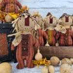 Group of primitive folk art scarecrow dolls with stitched faces, wool noses, homespun bodies, and fall gourd accents