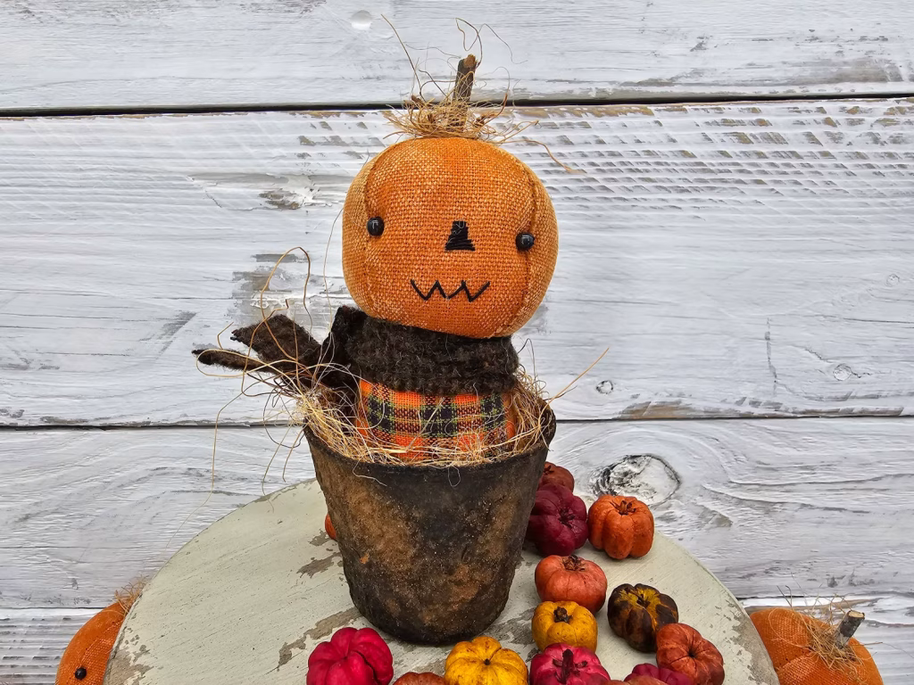 Primitive pumpkin shelf sitter with zig‑zag stitched mouth, aged osnaburg head, and real wood stem