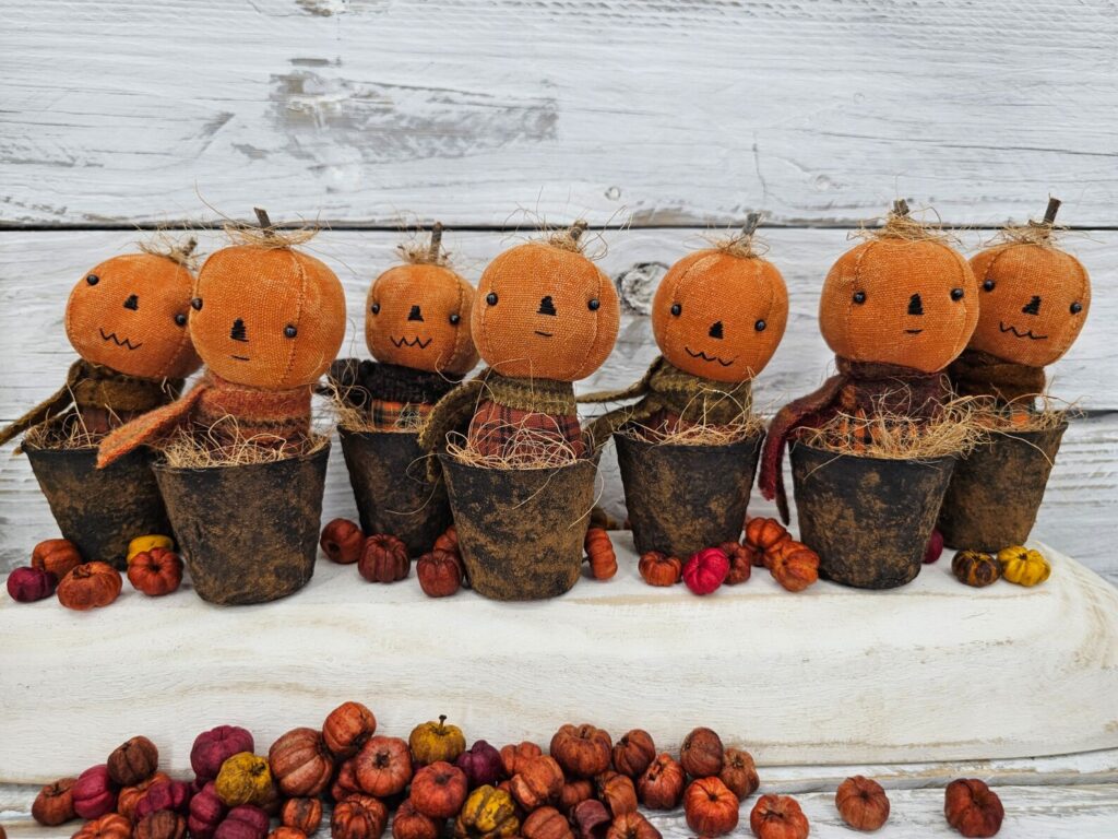 Handmade primitive pumpkins in faux rusty pots, each with aged osnaburg heads, wool scarves, and fall homespun bodies