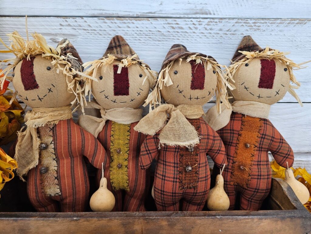 Group of primitive folk art scarecrow dolls with homespun bodies, wool noses, stitched faces, and fall gourd accents