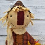 Close‑up of primitive folk art scarecrow showing stitched facial features, black bead eyes, and wool nose