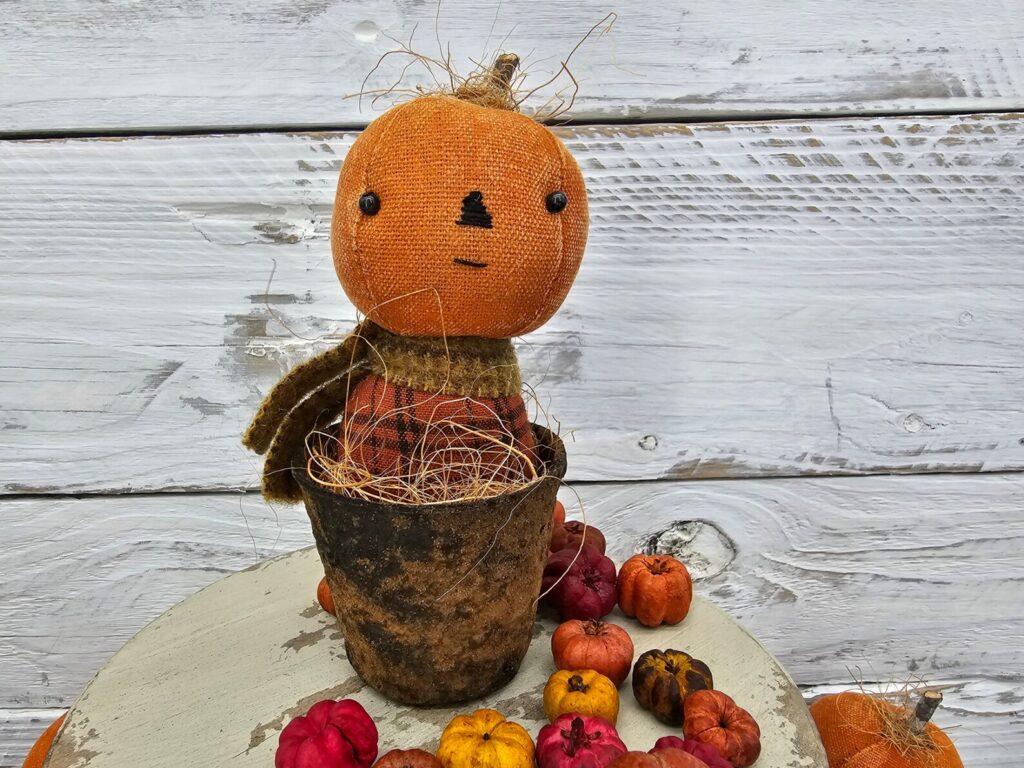 Primitive pumpkin shelf sitter with straight‑line stitched mouth, aged osnaburg head, and real wood stem