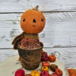 Primitive pumpkin shelf sitter with straight‑line stitched mouth, aged osnaburg head, and real wood stem