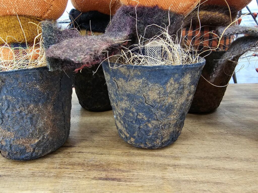 Close‑up of faux rusty pot painted black with cinnamon‑dusted aged finish and stuffed with fall straw