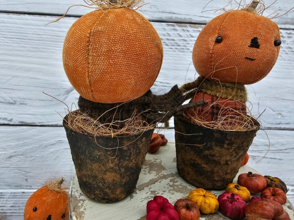 Back view of primitive pumpkin shelf sitter in faux rusty pot showing homespun fabric body and wool scarf