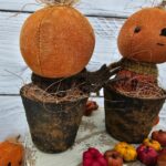 Back view of primitive pumpkin shelf sitter in faux rusty pot showing homespun fabric body and wool scarf