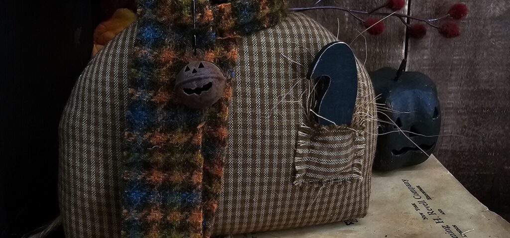 Close‑up of wooden black crow tucked in Oliver’s homespun pocket with fall straw accents.