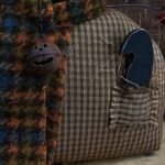 Close‑up of wooden black crow tucked in Oliver’s homespun pocket with fall straw accents.