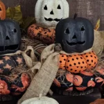 Close‑up of primitive Jack‑O‑Lantern stack pumpkins in four colors with aged paper‑mâché heads and fabric cushion bases