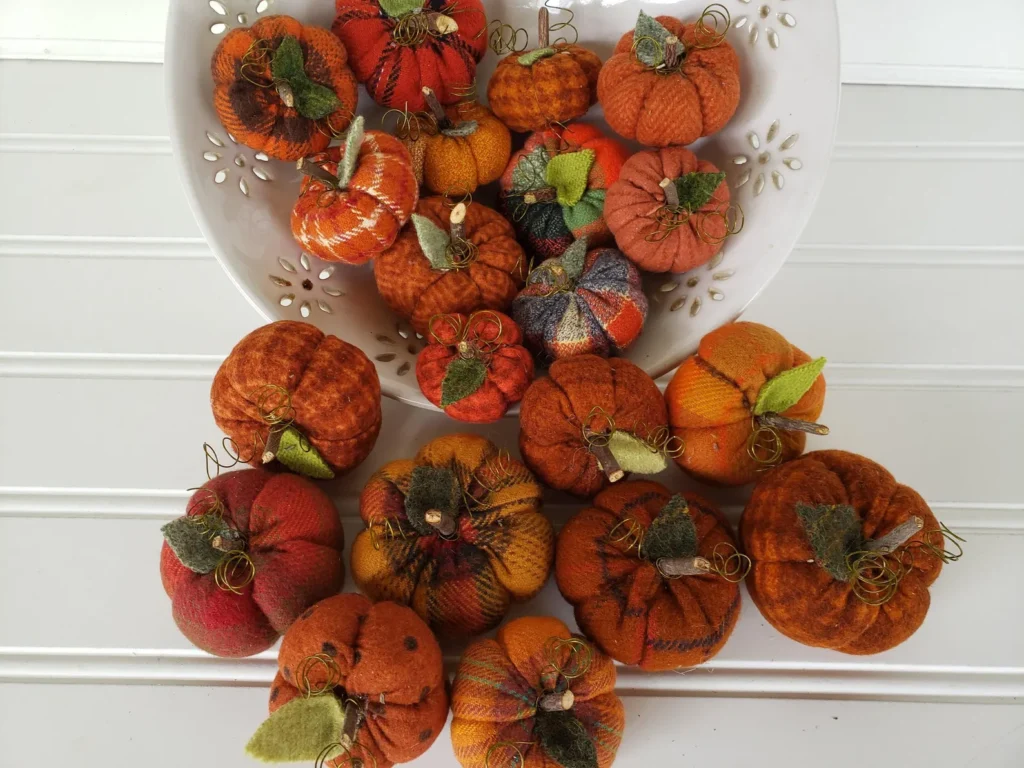 Mini flannel woolies pumpkins spilling out of a bowl, showing assorted autumn fabrics, wood stems, and wool leaves.