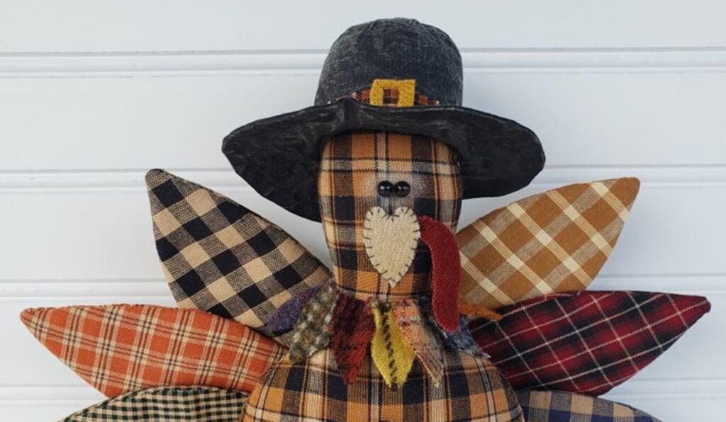 Close‑up of primitive homespun Thanksgiving turkey showing pilgrim hat, wool collar, and stitched facial details.