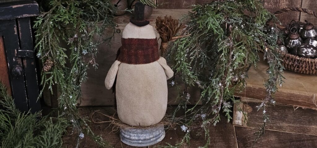 Back view of primitive snowman showing wool hat tie, aged osnaburg fabric, and winter folk‑art details.
