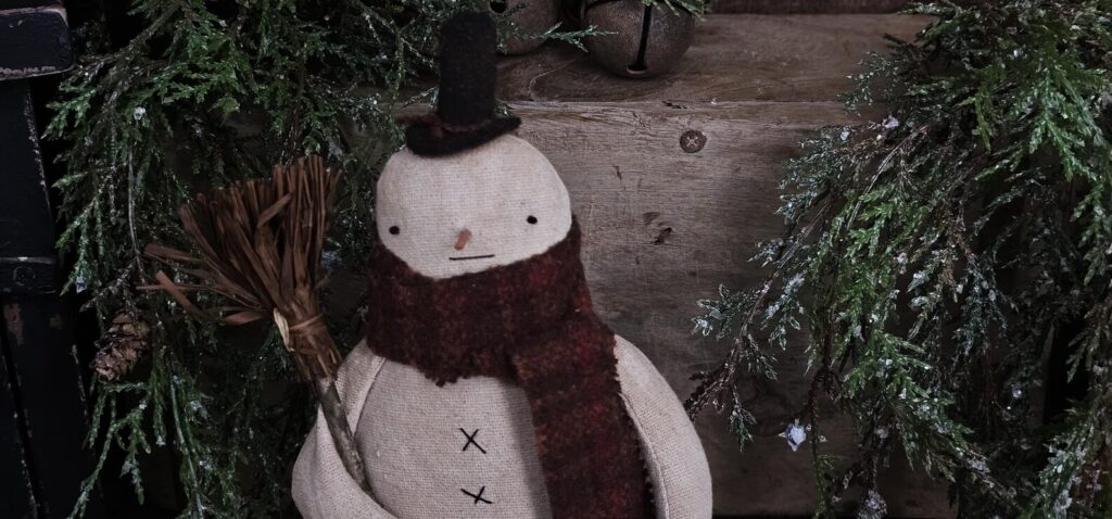 Top view of primitive snowman on Mason jar lid showing wool hat, wooden nose, and stitched face details.