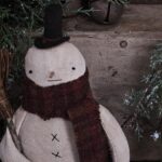 Top view of primitive snowman on Mason jar lid showing wool hat, wooden nose, and stitched face details.
