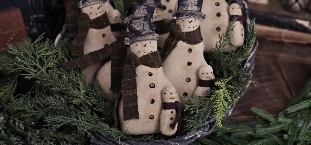 Primitive snowman tuck displayed as farmhouse Christmas décor on a tiered tray or shelf.