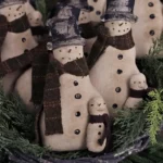Primitive snowman tuck displayed as farmhouse Christmas décor on a tiered tray or shelf.