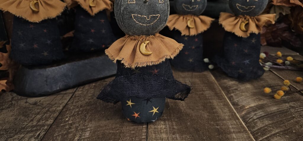 Primitive moon witch with star‑print Halloween body and terracotta homespun collar.