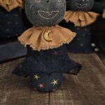 Primitive moon witch with star‑print Halloween body and terracotta homespun collar.